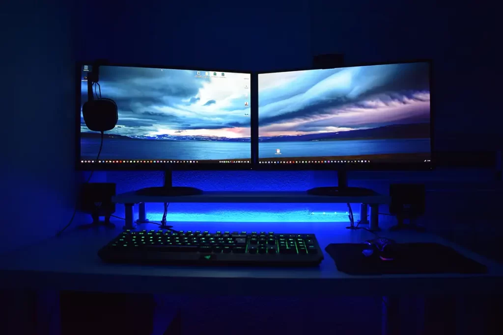 Two gaming monitors sitting on a desk with led lighting 