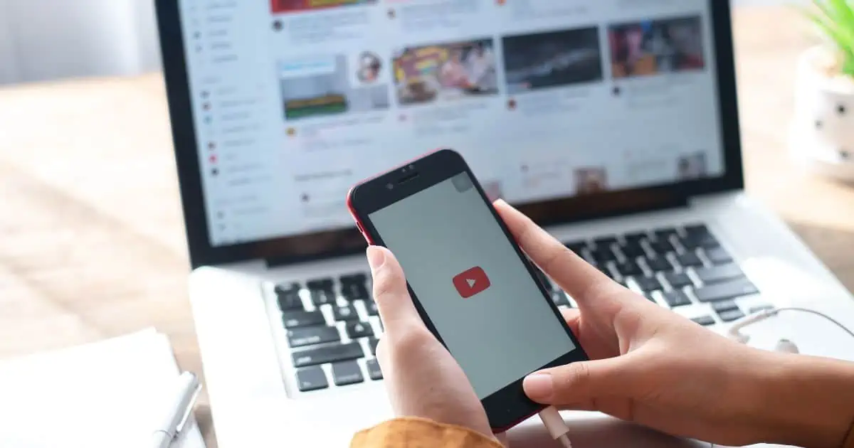 Iphone with a youtube logo and youtube on the laptop in the background